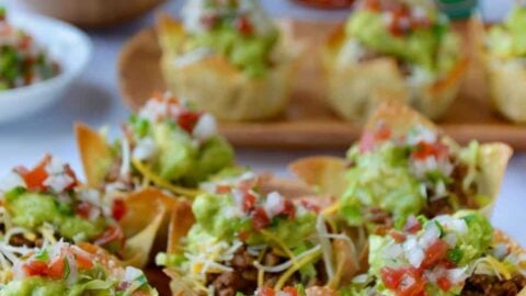 Easy Taco Salad Cups on a wood serving plate with hot sauce and guacamole in background