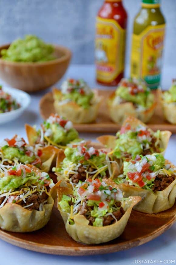 Easy Taco Salad Cups on a wood serving plate with hot sauce and guacamole in background