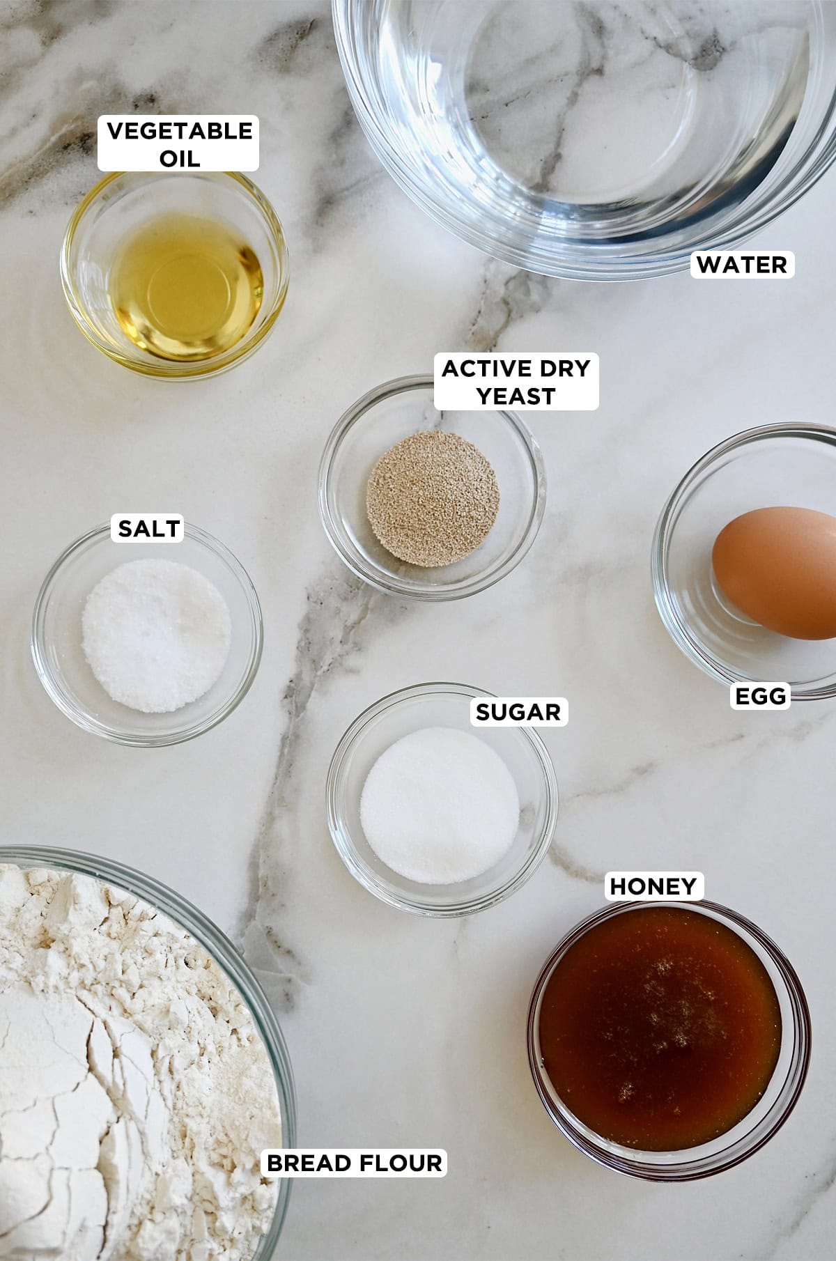 Ingredients to make homemade bagels: bread flour, active dry yeast, salt, sugar, honey, water, and an egg for an egg wash.