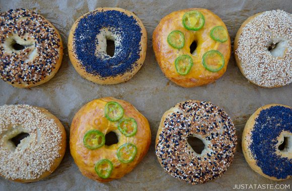 A baking sheet with two rows of bagels with assorted toppings