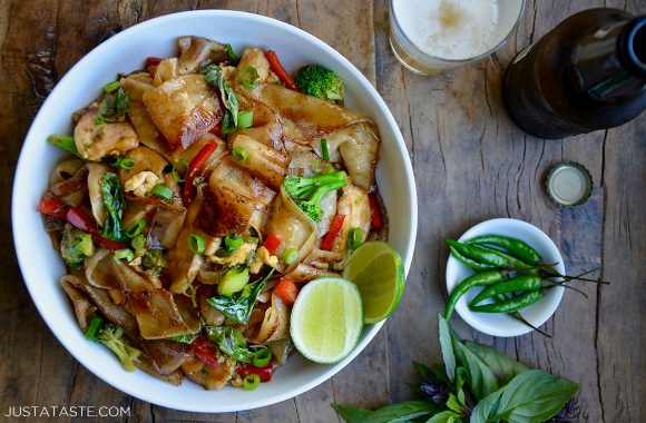 Homemade drunken noodles with chicken in white bowl next to herbs