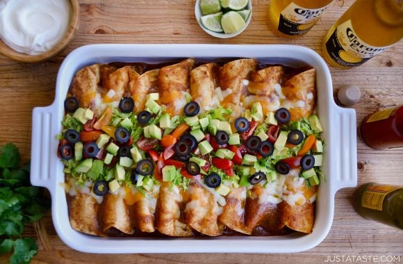A white baking dish filled with enchiladas topped with avocado and olives