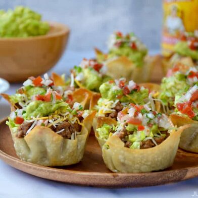 Homemade taco salad cups topped with guacamole and salsa on wood serving plate