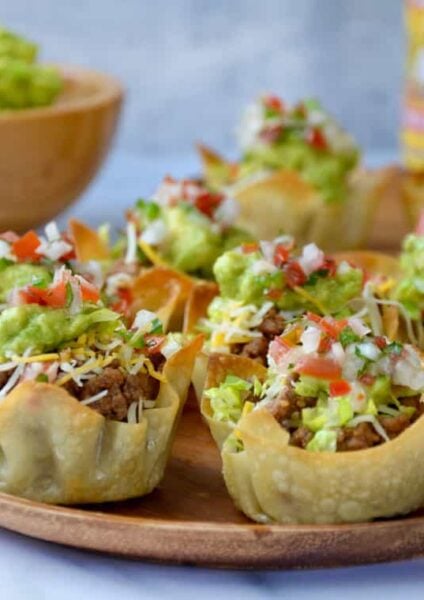 Homemade taco salad cups topped with guacamole and salsa on wood serving plate