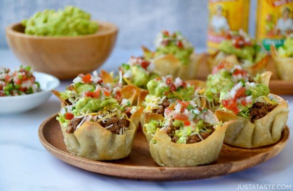 Homemade taco salad cups topped with guacamole and salsa on wood serving plate