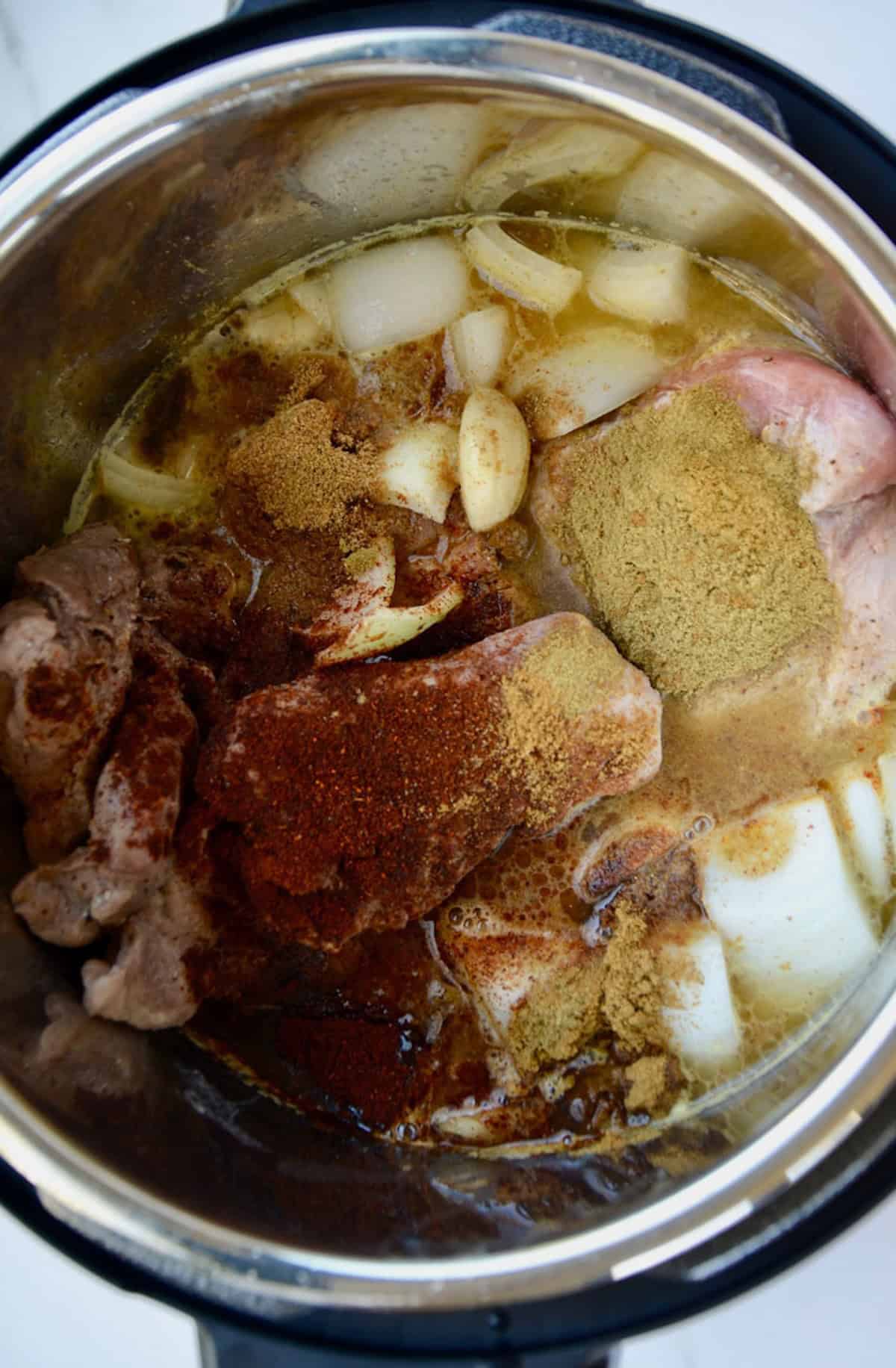 Making carnitas in an Instant Pot with garlic cloves, chopped onion, citrus juices and chicken stock.
