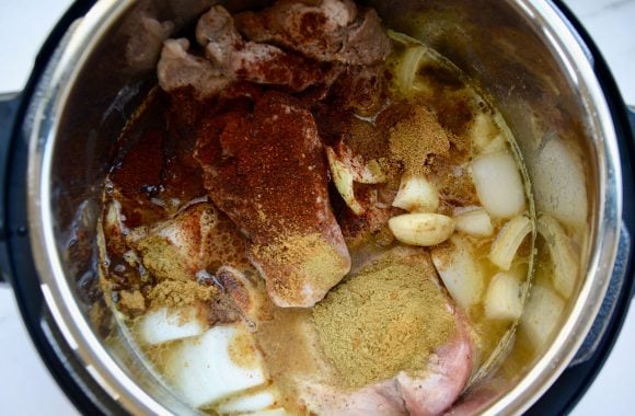 Top down view of an Instant Pot filled with carnitas ingredients: garlic, spices, boneless pork shoulder and onion