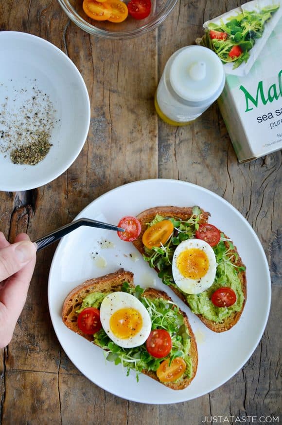 A white plate containing avocado hummus toast with jammy eggs and tomatoes