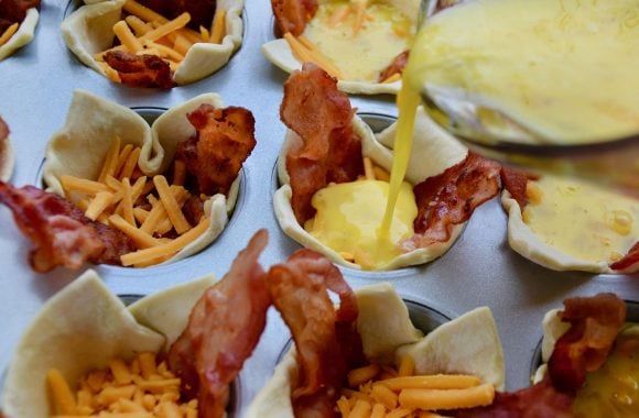 Pouring egg mixture into muffin tin cup containing puff pastry, bacon and cheese