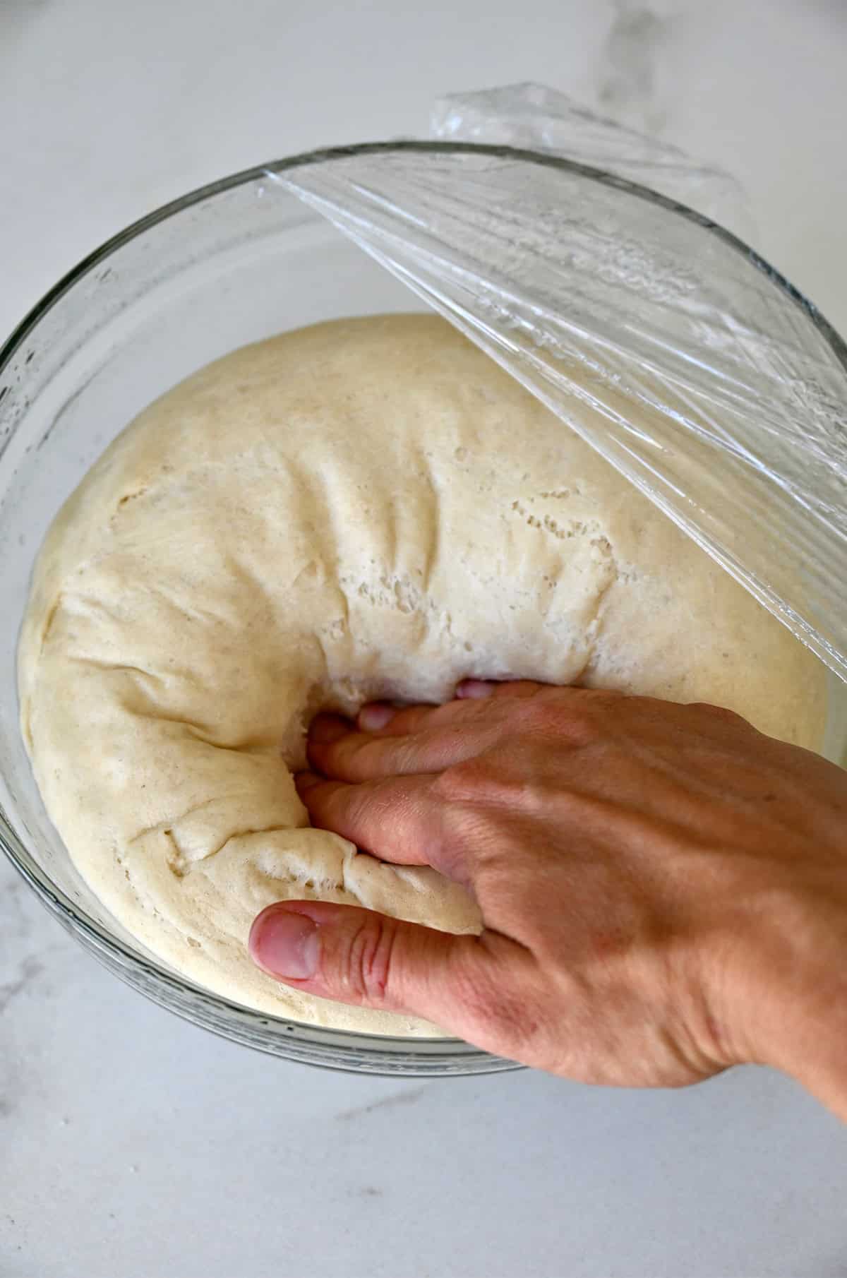 Punching down proofed dough in a bowl.