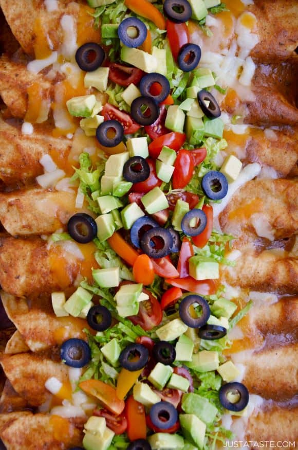 A close-up view of chicken enchiladas topped with avocado, olives and cheese