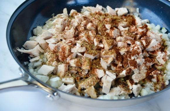A sauté pan filled with diced chicken, onions and spices