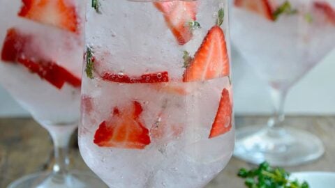 A clear glass containing sliced strawberries and crushed ice