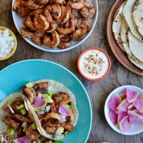 Top down view of spicy shrimp tacos, spicy shrimp, tortillas, sour cream, avocado and cilantro