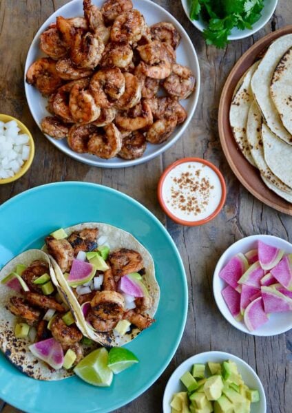 Top down view of spicy shrimp tacos, spicy shrimp, tortillas, sour cream, avocado and cilantro