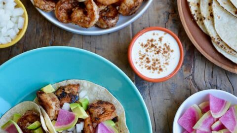 Top down view of spicy shrimp tacos, spicy shrimp, tortillas, sour cream, avocado and cilantro