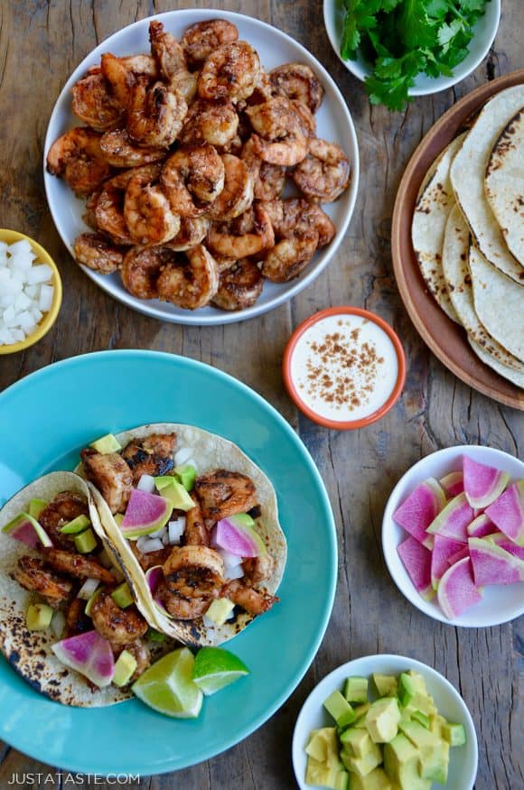 Top down view of spicy shrimp tacos, spicy shrimp, tortillas, sour cream, avocado and cilantro