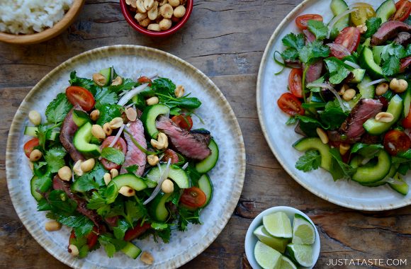 Two plates containing Thai Beef Salad next to two small bowls containing peanuts and limes 