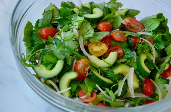 Glass bowl with Thai salad ingredients: cucumber, shallots, mint, cilantro and cherry tomatoes 