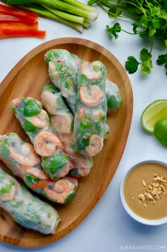 A wood serving plate containing Thai Spring Rolls with peanut sauce, limes and veggies around it