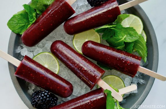 Boozy blackberry mojito popsicles over ice with limes and fresh mint