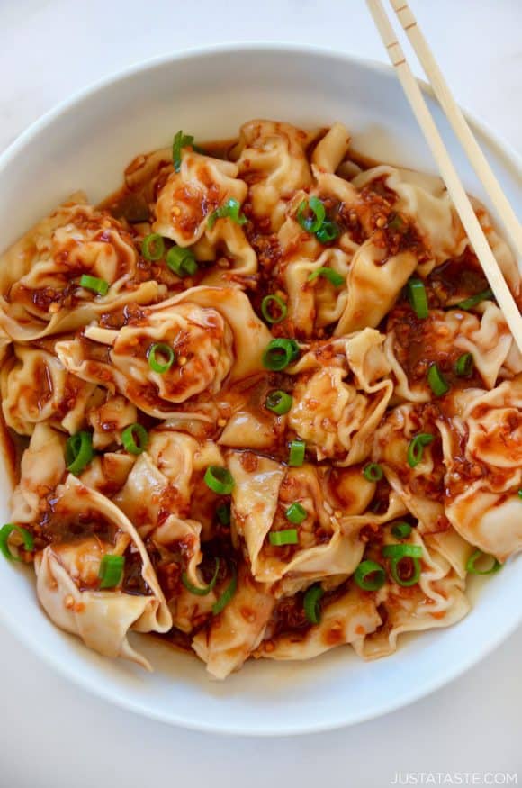 Top down view of white bowl containing spicy chicken wontons with chopsticks