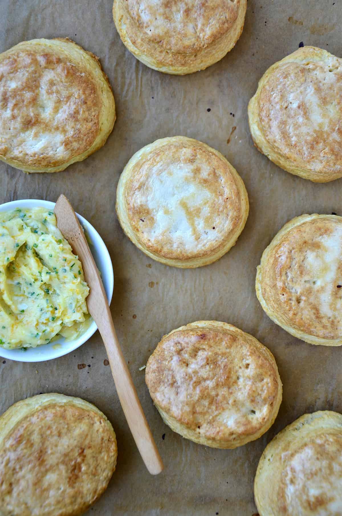 Buttermilk biscuits brushed with honey butter on a baking sheet with a small bowl containing honey butter.