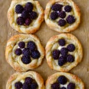 A baking sheet with brown parchment paper and blackberry cream cheese pastries.