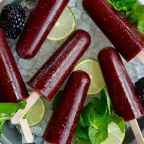Top down view of blackberry mojito popsicles over ice with limes and fresh mint