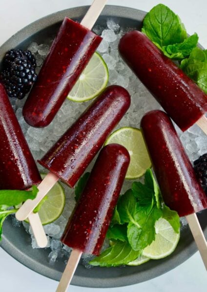 Top down view of blackberry mojito popsicles over ice with limes and fresh mint