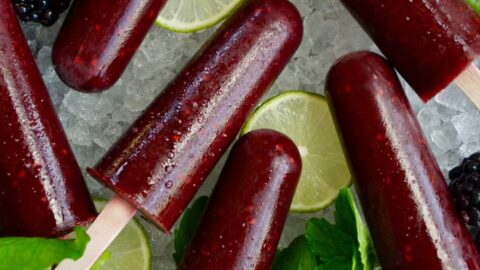 Top down view of blackberry mojito popsicles over ice with limes and fresh mint