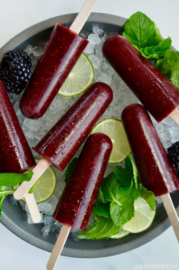 Top down view of blackberry mojito popsicles over ice with limes and fresh mint