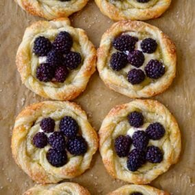 A baking sheet with brown parchment paper and blackberry pastries