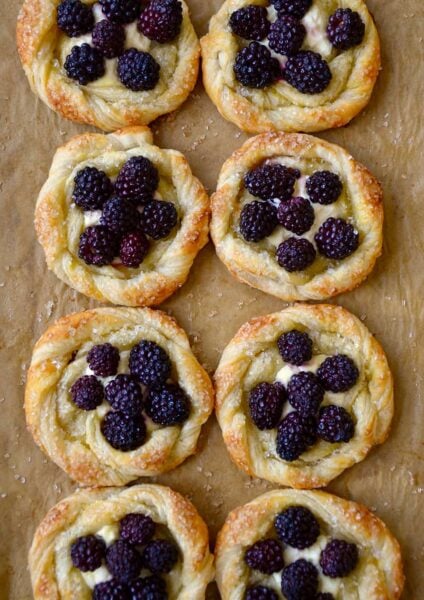 A baking sheet with brown parchment paper and blackberry pastries