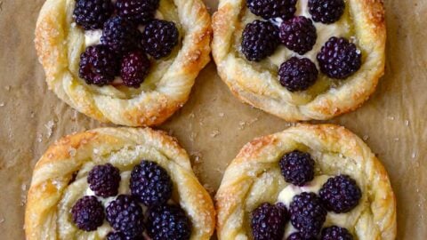 A baking sheet with brown parchment paper and blackberry pastries