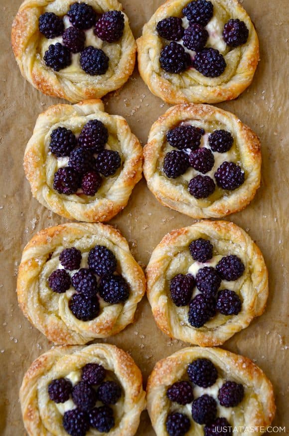 A baking sheet with brown parchment paper and blackberry pastries