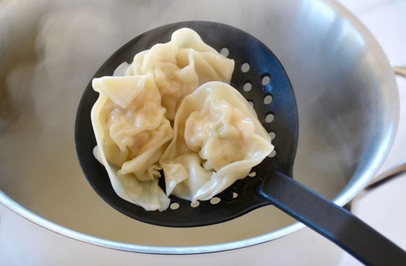 Slotted spoon with chicken wontons over large pot