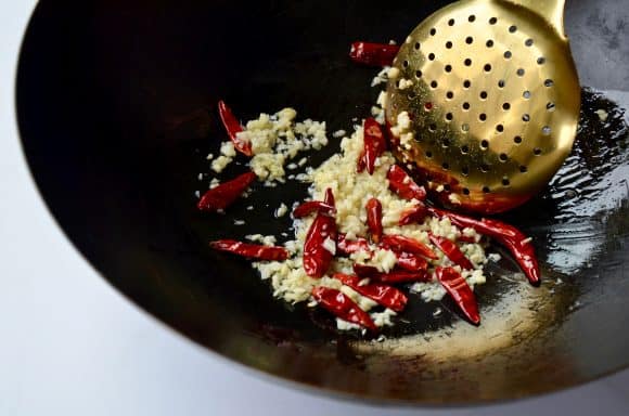 Stockpot containing minced garlic, ginger and whole chilies with slotted spoon