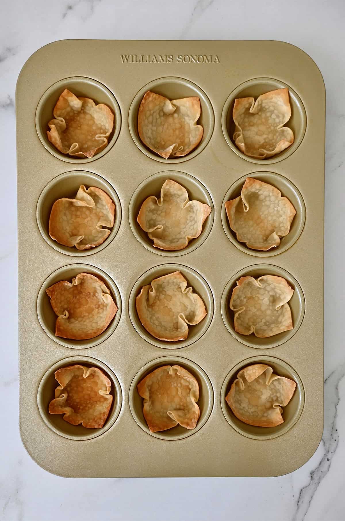 Golden brown and crispy baked wonton cups in a standard muffin pan.