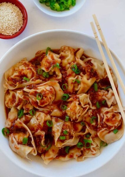 Bowl containing Spicy Chicken Wontons with chopsticks next to small red bowl with sesame seeds