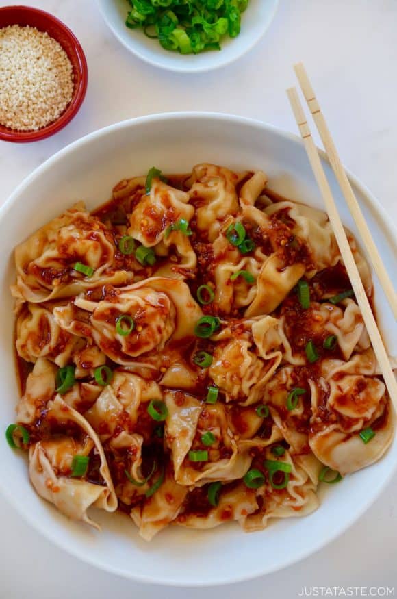 Bowl containing Spicy Chicken Wontons with chopsticks next to small red bowl with sesame seeds