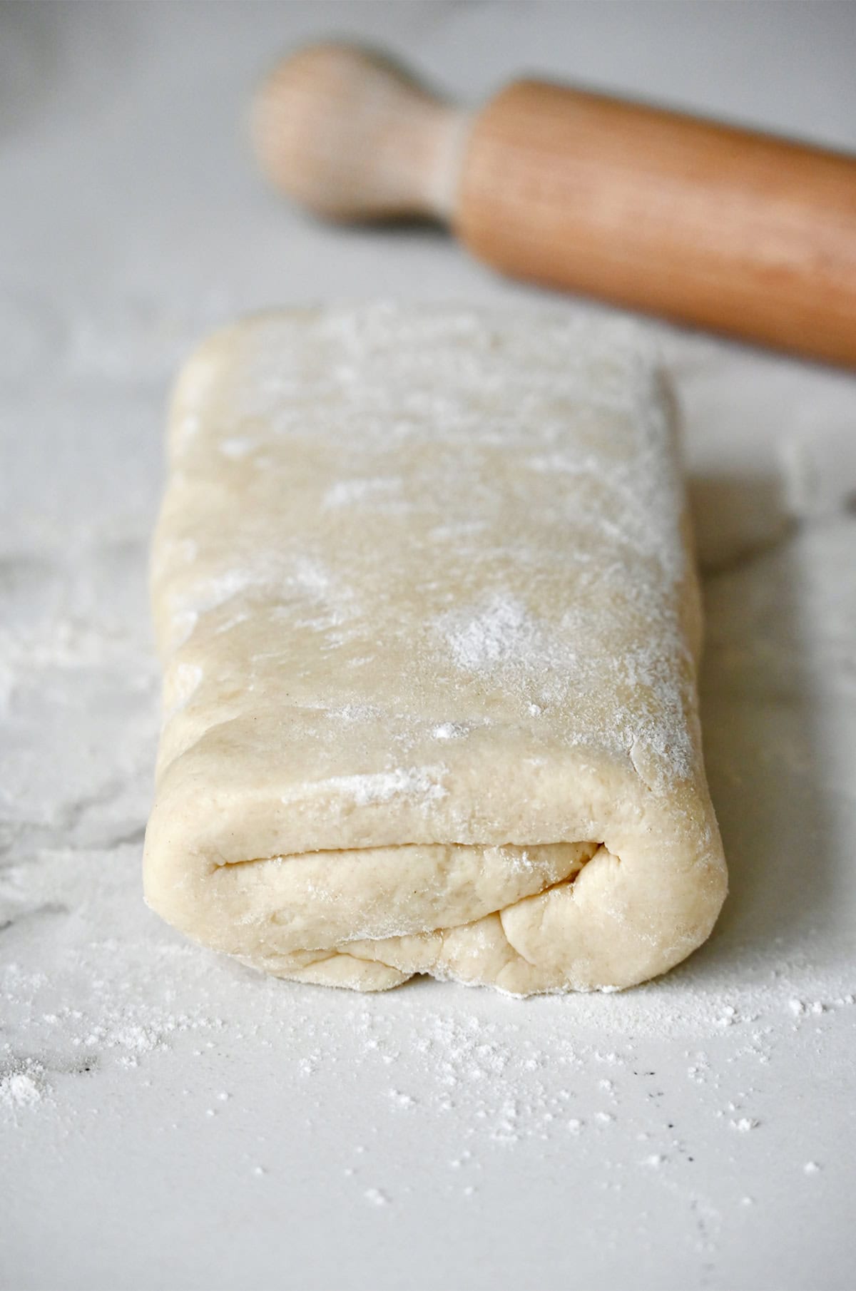 Folded biscuit dough on a lightly floured surface next to a rolling pin.