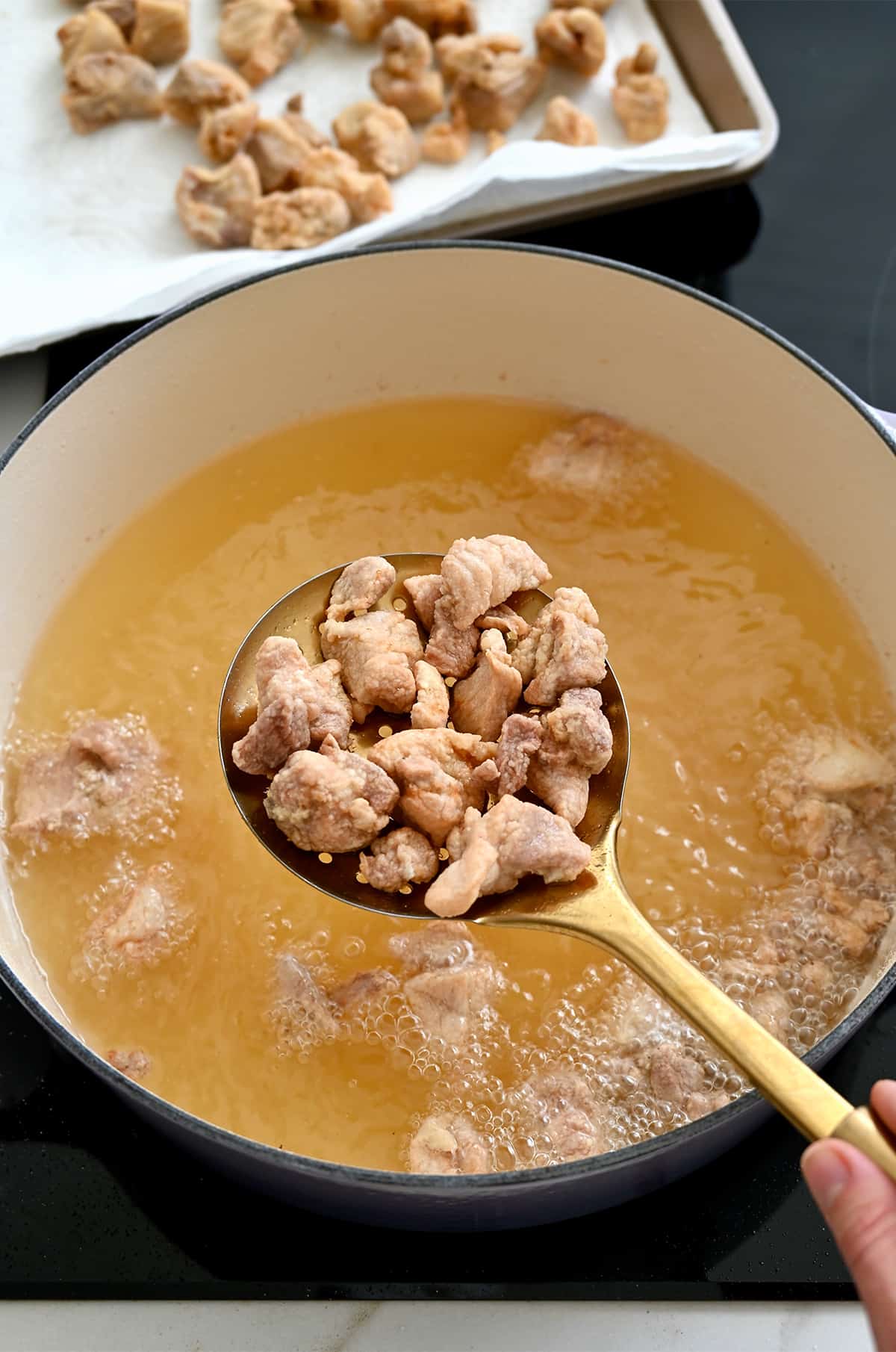 Deep-fried chicken pieces on a slotted spoon over a large Dutch oven containing sizzling vegetable oil.