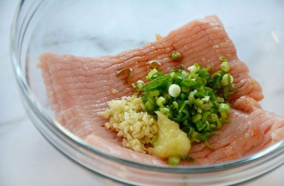 Glass bowl containing ground chicken, minced garlic and ginger, and scallions 