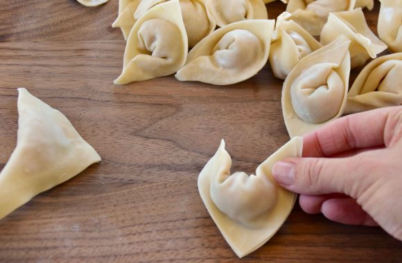 Hand shaping wontons on wood cutting board