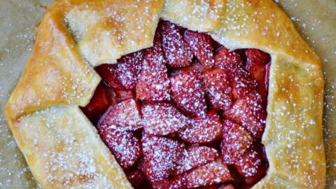 Strawberries and Cream Galette next to forks, bowl with whipped cream and sift containing powdered sugar