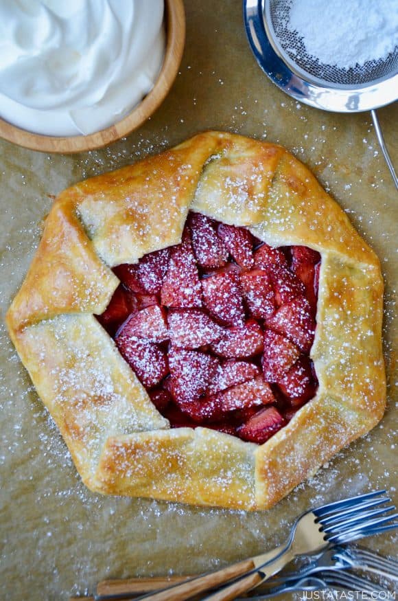 Strawberries and Cream Galette next to forks, bowl with whipped cream and sift containing powdered sugar