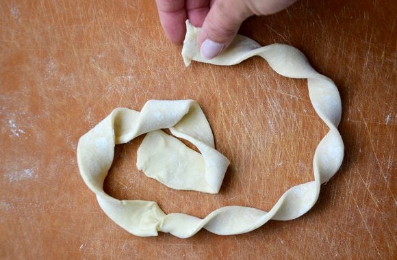 A cutting board containing puff pastry being twisted into a danish