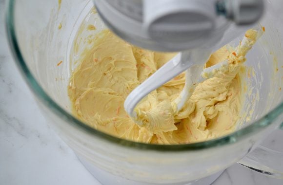 A clear mixing bowl containing cream cheese with orange zest