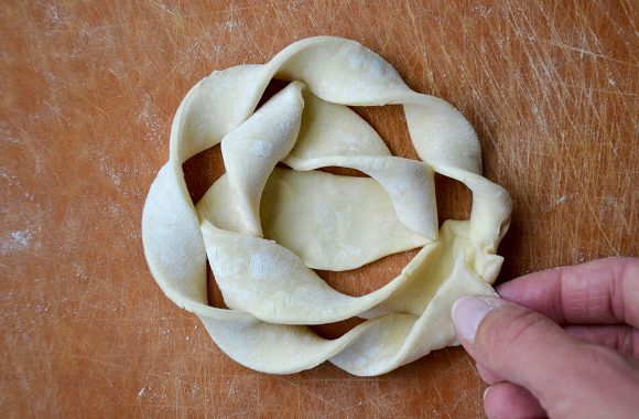 A close-up of a cutting board containing puff pastry being twisted into a danish